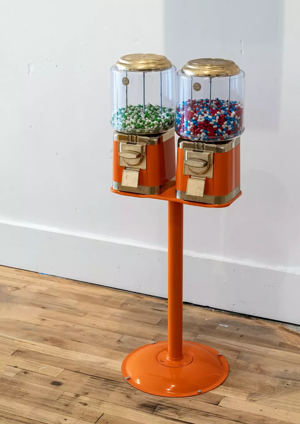 Gumball Machine, Gelatine Capsules, H:40.5&rdquo; x W:15&rdquo; x D:14&rdquo;, 2024 This installation features a gumball machine filled with Prozac and other psychotropic pills instead of candy, offering a stark commentary on the state of American healthcare. It critiques the ease with which psychiatric medications are prescribed and the influence of pharmaceutical companies, highlighting the troubling reality behind seemingly benign treatments and the commodification of mental health.