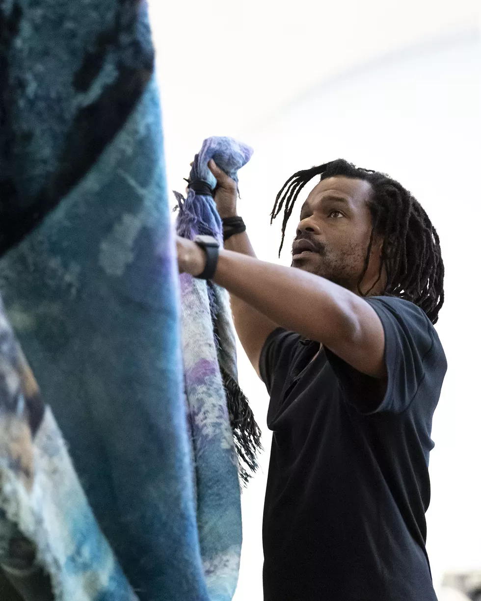 Noel W Anderson handles a suspended tapestry in the University Art Museum