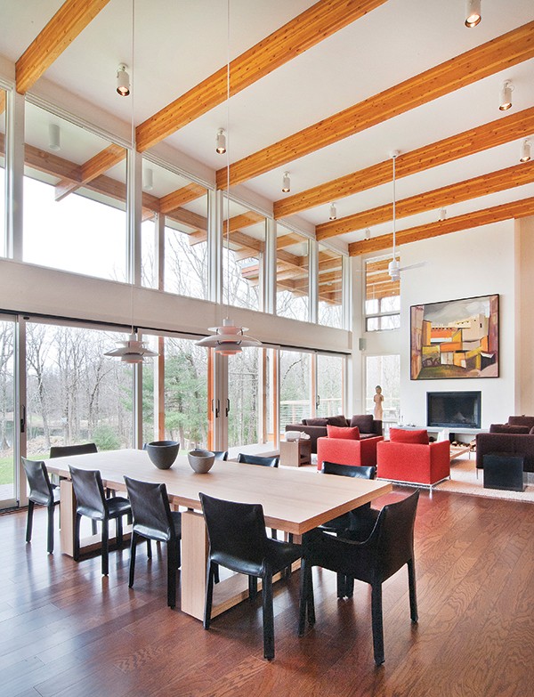 he dining area and great room’s two-story walls of glass overlook the private pond. The post-and-beam construction emphasizes the strength of the home.